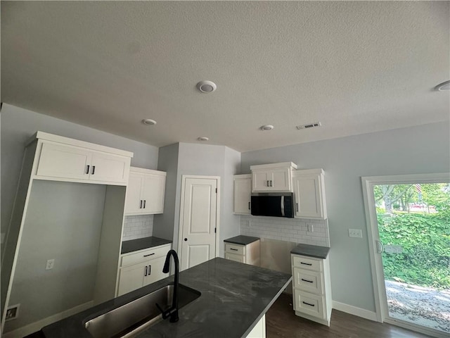324 E 2nd St, Adrian, MO 64720 - kitchen with dark countertops, stainless steel microwave, tasteful backsplash, white cabinetry, and a textured ceiling