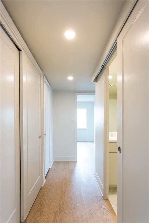 corridor featuring light wood-type flooring, recessed lighting, and baseboards