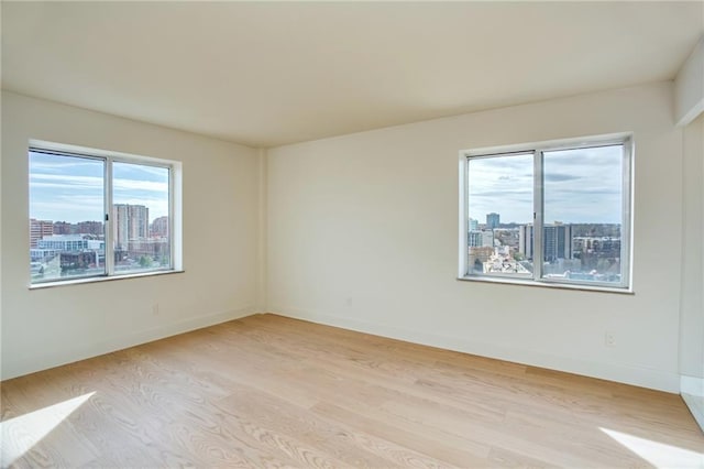empty room with light wood-type flooring, a city view, and baseboards