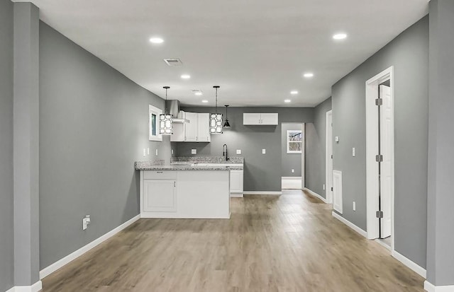 kitchen with white cabinetry, a peninsula, light wood-style flooring, wall chimney range hood, and baseboards