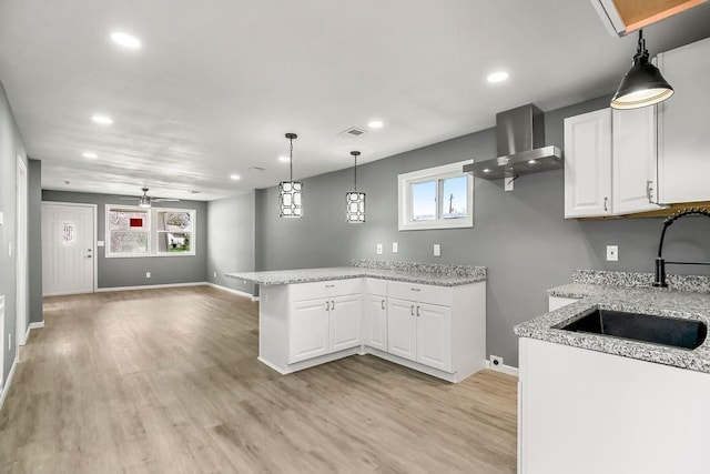kitchen with light wood-type flooring, a sink, white cabinets, a peninsula, and wall chimney exhaust hood