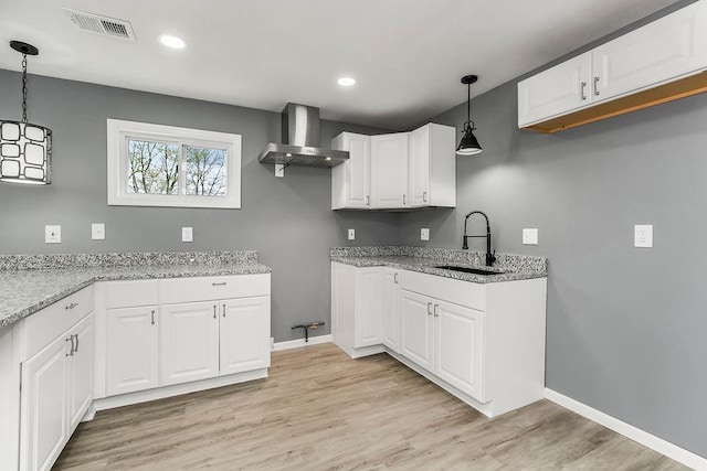 kitchen featuring visible vents, a sink, wall chimney exhaust hood, and light stone counters