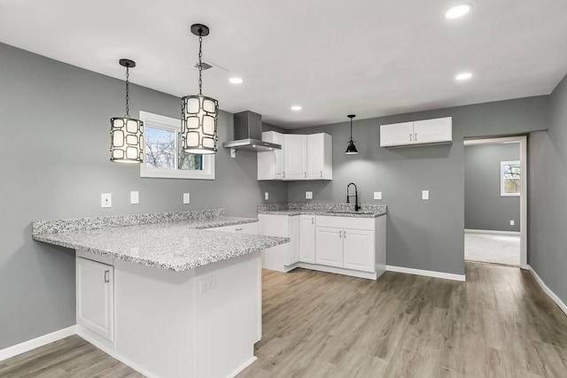 kitchen featuring wall chimney range hood, light wood-type flooring, light stone countertops, and a sink