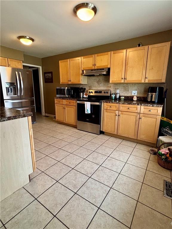 1519 Niagara St, Burlington, KS 66839 - kitchen featuring tasteful backsplash, light tile patterned floors, stainless steel appliances, under cabinet range hood, and dark countertops