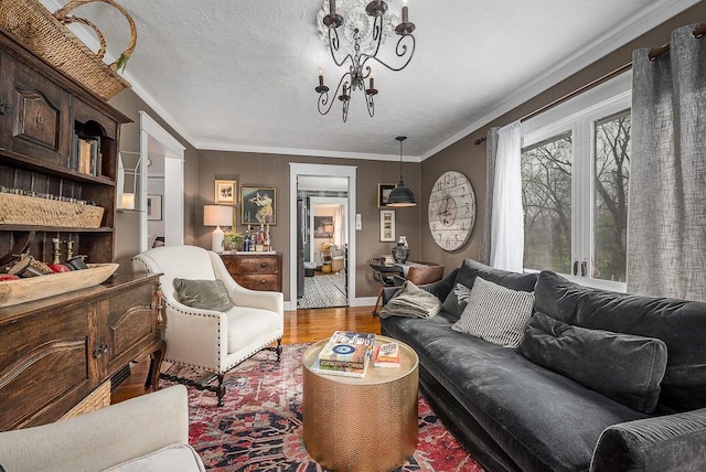 living room with a textured ceiling, crown molding, baseboards, wood finished floors, and an inviting chandelier