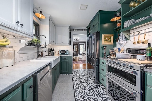 kitchen with green cabinets, light countertops, decorative backsplash, a sink, and appliances with stainless steel finishes