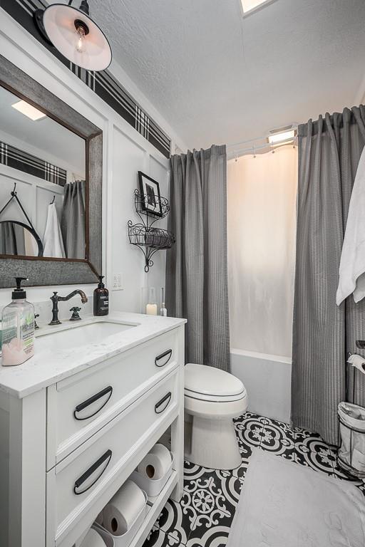 full bath with toilet, vanity, shower / bathtub combination with curtain, a textured ceiling, and tile patterned flooring