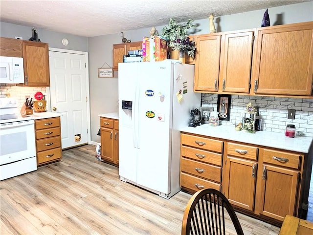 kitchen with white appliances, light wood-style floors, light countertops, a textured ceiling, and backsplash