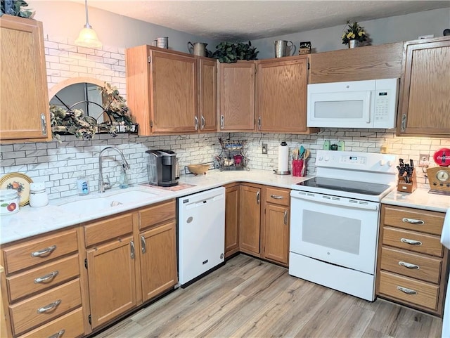 kitchen featuring decorative backsplash, white appliances, light countertops, a sink, and light wood finished floors