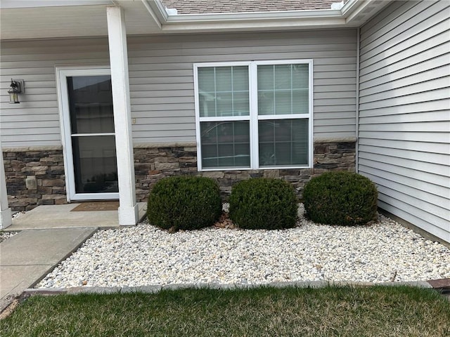 doorway to property featuring stone siding and roof with shingles