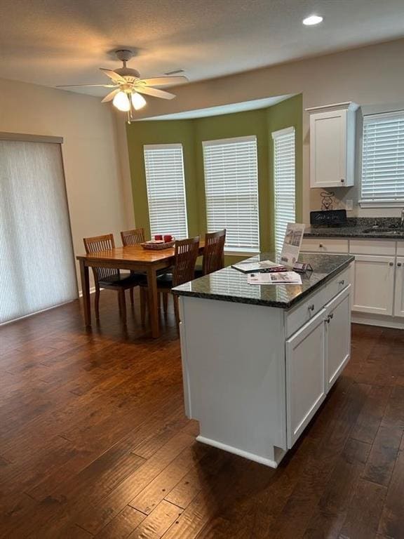 kitchen with dark wood-type flooring, white cabinets, ceiling fan, and a center island