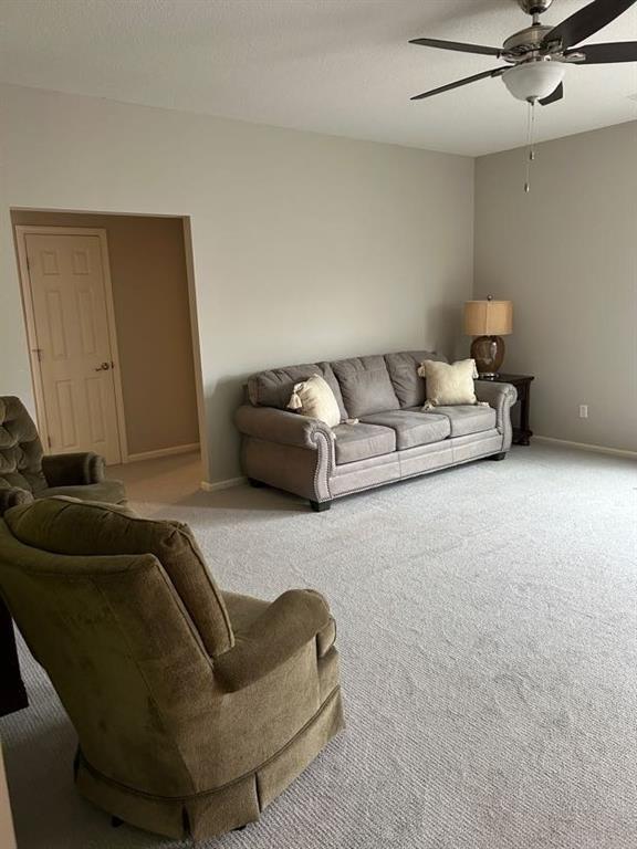 living area featuring light carpet, baseboards, and ceiling fan