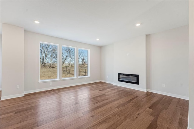 503 Woodview Dr, Raymore, MO 64083 - unfurnished living room featuring wood finished floors, a glass covered fireplace, baseboards, and recessed lighting