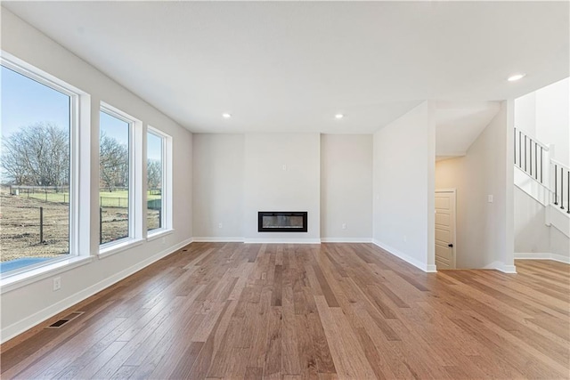 503 Woodview Dr, Raymore, MO 64083 - unfurnished living room featuring wood finished floors, stairs, a glass covered fireplace, baseboards, and recessed lighting