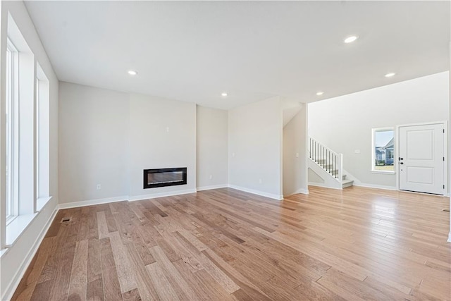 503 Woodview Dr, Raymore, MO 64083 - unfurnished living room with stairway, light wood finished floors, a glass covered fireplace, recessed lighting, and baseboards