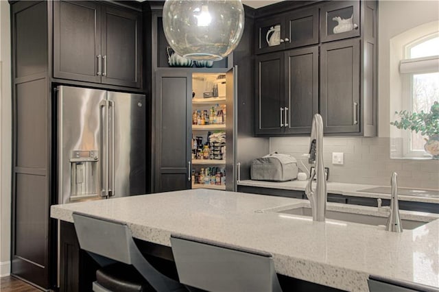 kitchen featuring light stone countertops, glass insert cabinets, high quality fridge, tasteful backsplash, and a sink