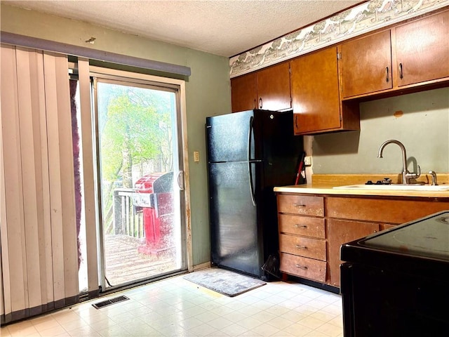kitchen with visible vents, light countertops, brown cabinets, a sink, and black appliances