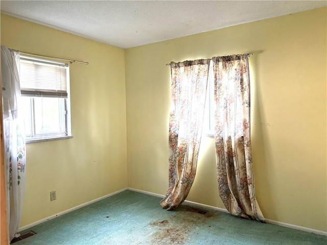 unfurnished room with carpet flooring, a textured ceiling, baseboards, and visible vents