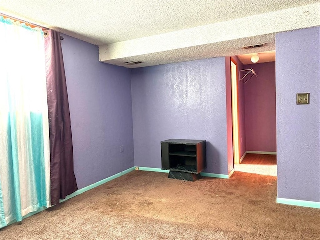 carpeted spare room featuring baseboards, a textured wall, a textured ceiling, and visible vents