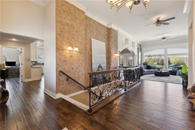 hallway featuring dark wood-style flooring, arched walkways, an upstairs landing, and crown molding
