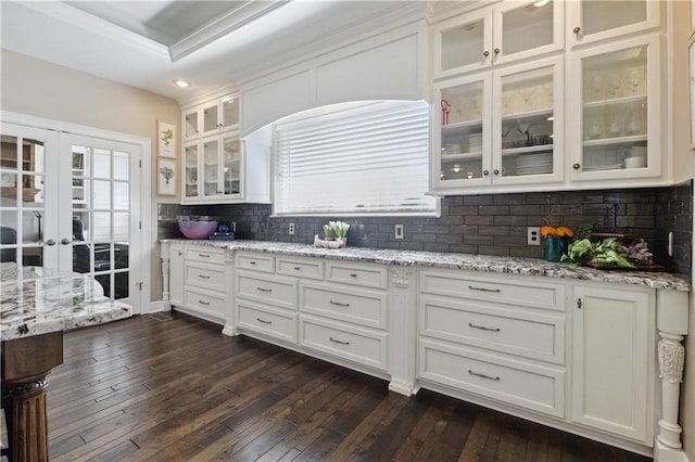kitchen featuring white cabinets, light stone counters, french doors, glass insert cabinets, and dark wood-style flooring