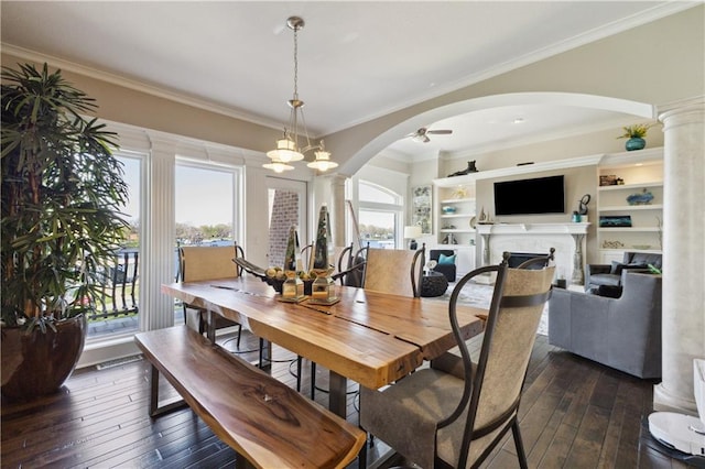 dining area featuring ornate columns, arched walkways, dark wood-type flooring, crown molding, and a fireplace