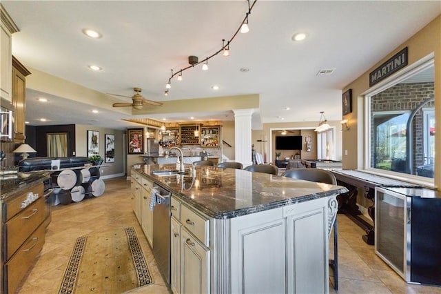 kitchen with an island with sink, stainless steel dishwasher, a sink, open floor plan, and ceiling fan