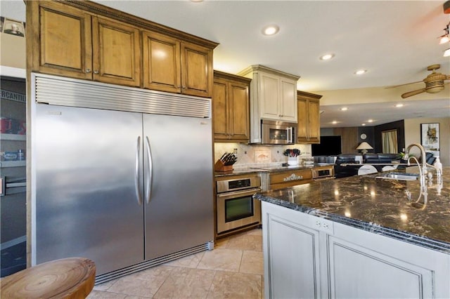 kitchen featuring dark stone countertops, a sink, decorative backsplash, appliances with stainless steel finishes, and open floor plan