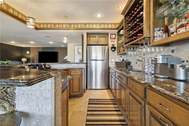 kitchen featuring brown cabinets, a sink, freestanding refrigerator, dark stone counters, and tasteful backsplash