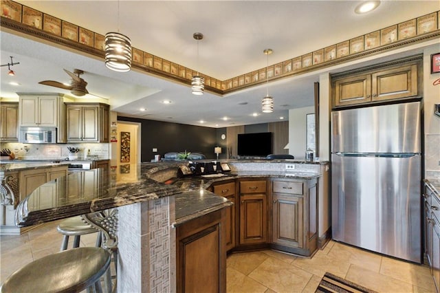 kitchen featuring stainless steel appliances, dark stone counters, tasteful backsplash, ceiling fan, and decorative light fixtures
