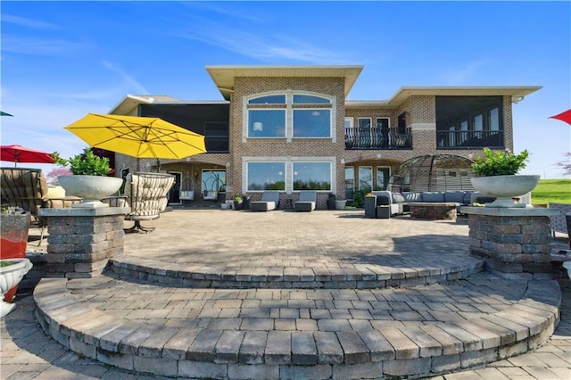 rear view of house with brick siding, an outdoor living space with a fire pit, a balcony, and a patio