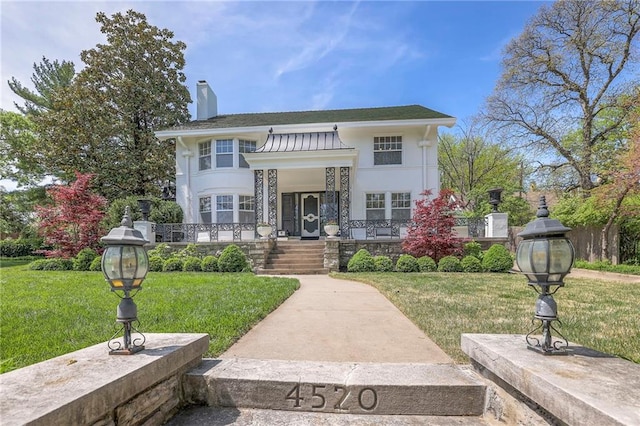 view of front of home featuring a standing seam roof, a chimney, a porch, and a front lawn
