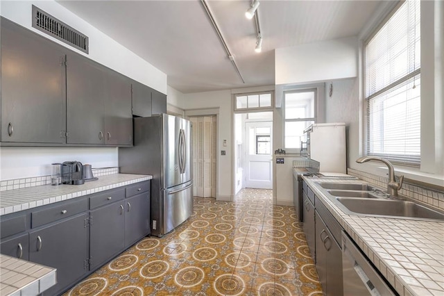 kitchen with visible vents, tile countertops, a sink, and appliances with stainless steel finishes