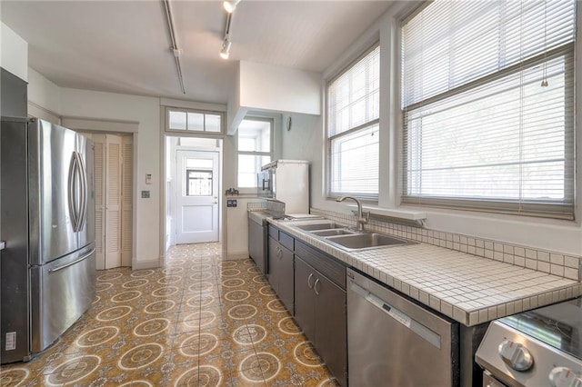 kitchen featuring appliances with stainless steel finishes, a sink, rail lighting, a healthy amount of sunlight, and light floors