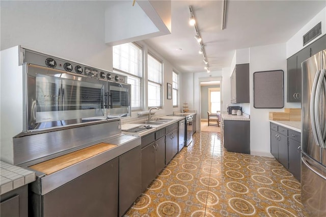 kitchen with track lighting, freestanding refrigerator, visible vents, light countertops, and a sink