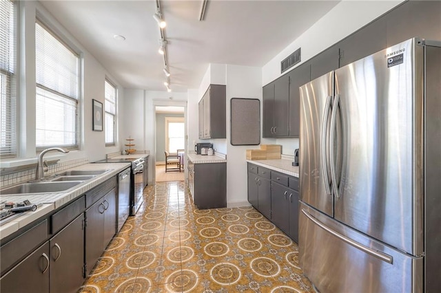 kitchen featuring track lighting, a sink, light countertops, stainless steel appliances, and visible vents