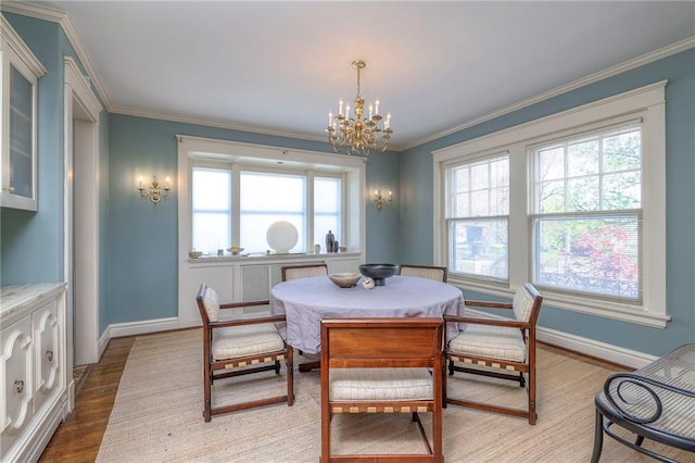 dining room featuring baseboards, ornamental molding, light wood finished floors, and a notable chandelier