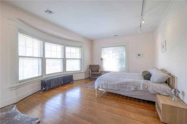 bedroom featuring rail lighting, radiator heating unit, wood finished floors, visible vents, and ornamental molding