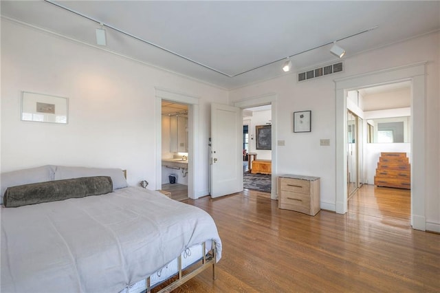 bedroom featuring visible vents, rail lighting, ensuite bath, and wood finished floors