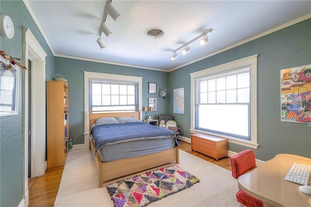 bedroom with visible vents, wood finished floors, track lighting, a baseboard heating unit, and ornamental molding