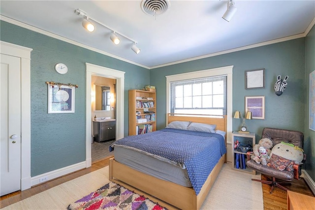 bedroom with track lighting, visible vents, ornamental molding, and wood finished floors