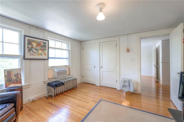 interior space with baseboards, multiple windows, radiator, and light wood-style floors