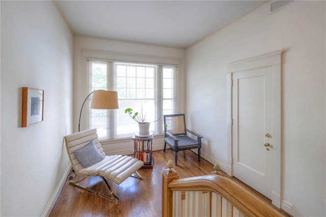 living area featuring baseboards, visible vents, ornamental molding, and wood finished floors