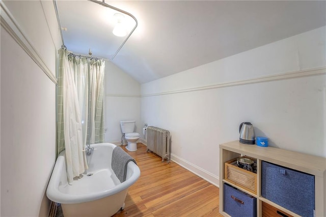 bathroom featuring toilet, radiator heating unit, baseboards, wood finished floors, and vaulted ceiling