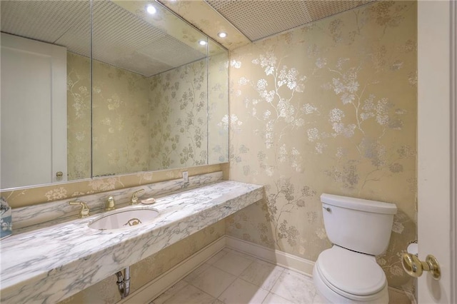 bathroom featuring a sink, toilet, recessed lighting, baseboards, and wallpapered walls