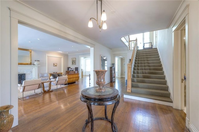 interior space featuring an inviting chandelier, a fireplace, baseboards, wood finished floors, and ornamental molding