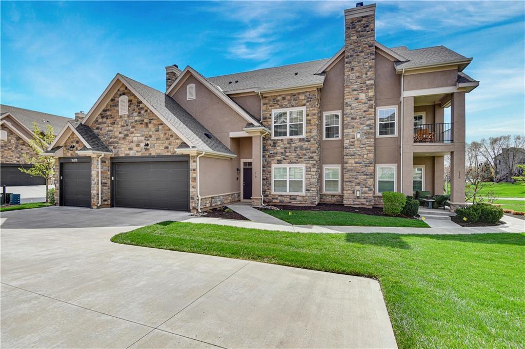 view of front of home featuring stucco siding, an attached garage, stone siding, a front lawn, and a chimney