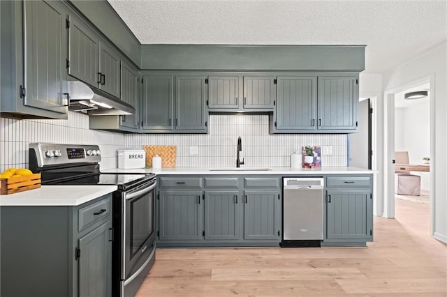 14875 Edgerton Rd, Gardner, KS 66030 - kitchen with appliances with stainless steel finishes, under cabinet range hood, light wood-style floors, tasteful backsplash, and a textured ceiling