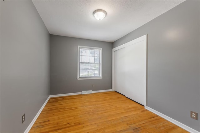 7201 E 130th Ter, Grandview, MO 64030 - unfurnished bedroom with light wood-style flooring, a closet, and a textured ceiling