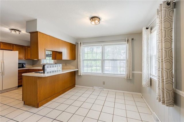 7201 E 130th Ter, Grandview, MO 64030 - kitchen with freestanding refrigerator, brown cabinets, a peninsula, light countertops, and healthy amount of natural light